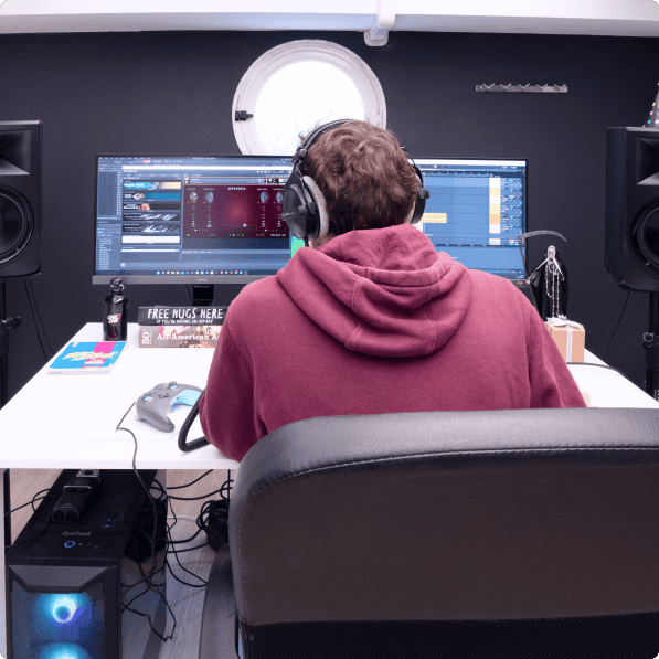 A person wearing headphones working at a desk with dual monitors displaying music production software, in a modern workspace.