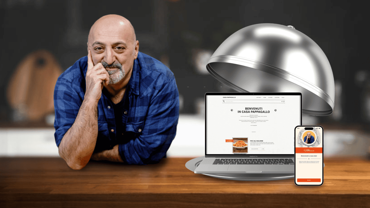 Luca Pappagallo in cucina con un computer portatile che mostra il sito web di Casa Pappagallo e uno smartphone che mostra l'interfaccia dell'app.