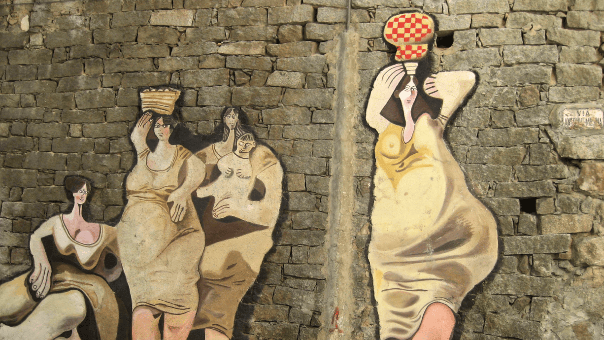 Street art depicting stylized women on a stone wall in Sardinia, showcasing cultural and artistic heritage.